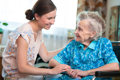 Elderly woman sitting in wheel chair next to caregiver image